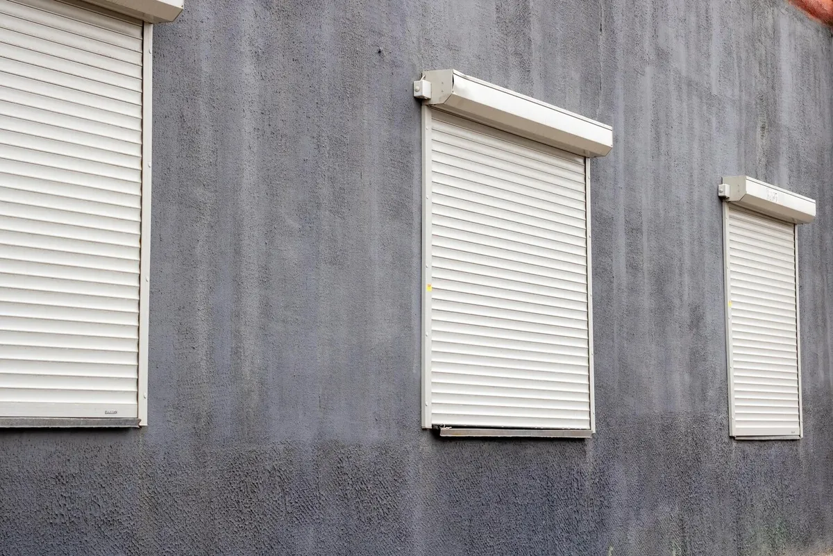 Trois volets roulants blancs fermés avec coffres extérieurs de rénovation posés sur une façade grise, photo d'illustration