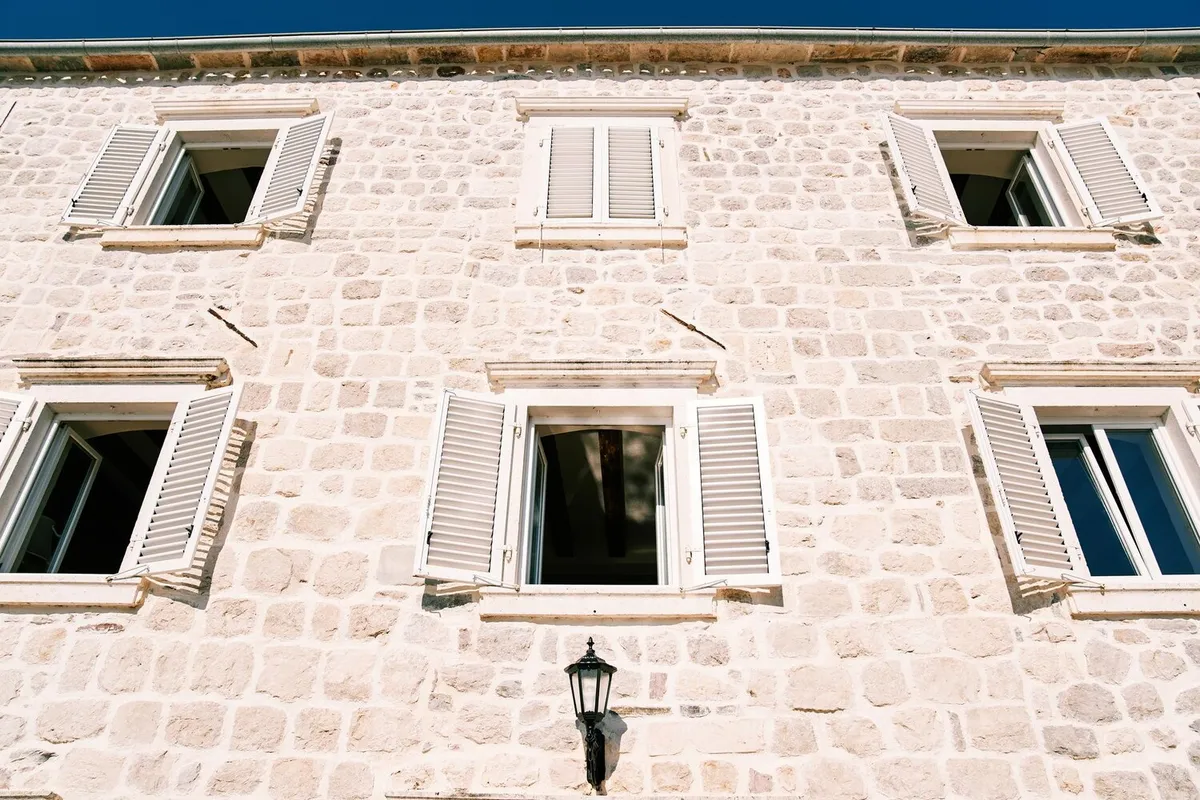 Façade en pierre calcaire claire avec fenêtres à persiennes en bois peint blanc, photo d'illustration